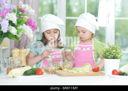 Due adorabili bambine in grembiuli preparare deliziose insalate Foto Stock