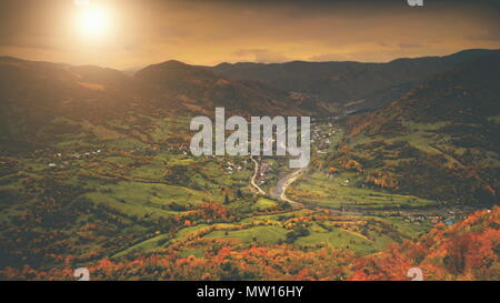 Vista aerea: bellissimo canyon villaggio situato lungo il fiume. Autunno drammatico paesaggio di montagna con prati verdi, arancione la pineta, tramonto cielo nuvoloso. Carpazi, Ucraina, l'Europa. Foto Stock