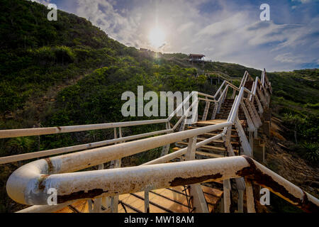 In cemento e le scale di acciaio in una pericolosa condizione di abbandono portano su un pendio verso rifugi e il sole di setting. Perhentian island, Malaysia. Foto Stock