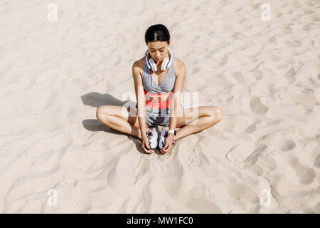 Slim asian sportive con cuffie stiramento sulla sabbia Foto Stock
