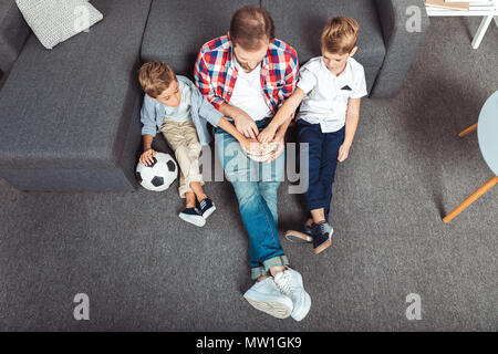 Elevato angolo di visione del padre con figli mangiare popcorn mentre si guarda la partita di calcio a casa Foto Stock