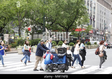 Senzatetto uomo spinge un carrello pieno di belongoings e lattine di soda attraverso la sesta strada sulla 34th Street in Manhattan. Foto Stock