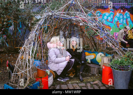 Due donne sono seduti sotto la tenda artistiche fatte di rami degli alberi presso la comunità di nomadi giardino off Brick Lane nella zona est di Londra, Regno Unito. Foto Stock