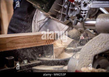 Chiusura del falegname esperto in abiti da lavoro e piccole buiness proprietario lavorando nel laboratorio di falegnameria, utilizzando una sega circolare per tagliare attraverso un di legno p Foto Stock