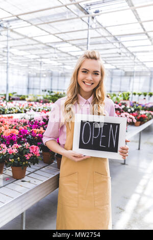 Donna sorridente proprietario del Glasshouse azienda scheda aperta da fiori in serra Foto Stock