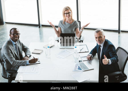 Happy business multietnica gente seduta a tavola e sorridente alla telecamera durante la riunione di successo Foto Stock