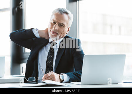 Imprenditore senior che soffrono di dolore al collo mentre si lavora con il computer portatile Foto Stock