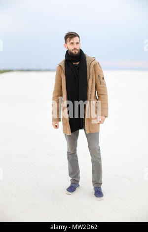 Uomo bello indossare cappotto e sciarpa in piedi nel bianco della neve sullo sfondo. Foto Stock