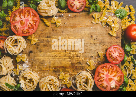 Varie la pasta cruda di verdure fresche e il verde delle foglie sparse intorno al tagliere di legno come spazio di copia Foto Stock