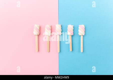 Diversi colori pastello marshmallows su bastoni sul rosa pastello blu sfondo con copia spazio. Vista dall'alto. Concettuale Trend alimentari laici piatta Foto Stock