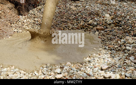 Terreno liquido viene versato dal mescolatore concreto sul pavimento del pozzo di scavo coperto con ghiaia grossa e pietre, Germania Foto Stock