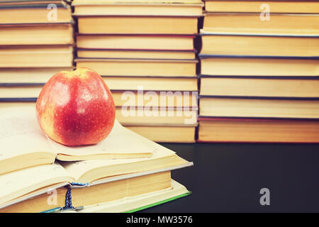 Red apple sul libro aperto contro lo sfondo di libri Foto Stock