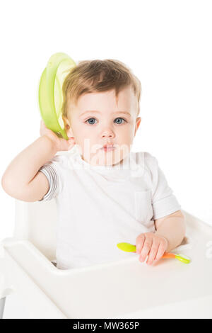 Bambino seduto nel seggiolone con piastra e cucchiaio isolati su sfondo bianco Foto Stock
