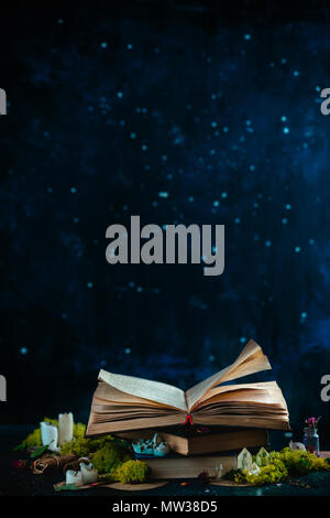 Libro aperto con candele, cristalli e Moss. Lettura del concetto di fantasia con copia spazio. Magica ancora in vita su uno sfondo scuro con apparecchiature occulto. Foto Stock