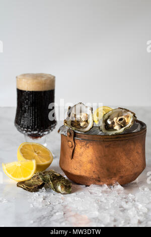 Ostriche crude in ghiaccio in un secchio di rame con limone e un bicchiere di birra stout Foto Stock