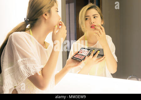 Bella asiatica ragazza adolescente rossetto la sua bocca prima lo specchio nella stanza da bagno Foto Stock