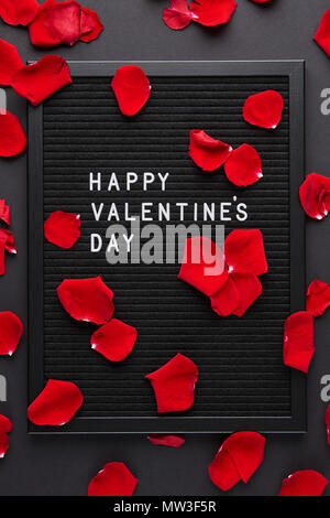 Letterboard nero bianco con lettere in plastica con citazione Buon San Valentino, con petali di rosa su sfondo nero. Foto Stock