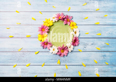 Piastra verde circondato da giallo, bianco e pink gerbera fiori su uno sfondo blu Foto Stock