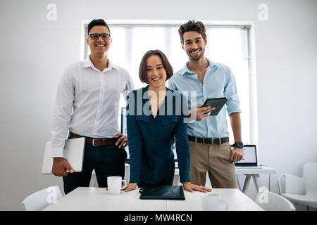 La gente di affari in piedi in sala conferenze azienda laptop e tablet. Il team di sorridere per gli sviluppatori di applicazioni in piedi nella sala riunioni in ufficio Foto Stock