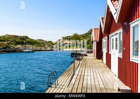 Red cabine in una fila su un molo in legno e con la locale spiaggia balneare in background. Ronnang sull'isola Tjorn, Svezia. Foto Stock