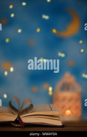 Il libro sacro del Corano su una superficie di legno. Notte Blu cielo con luna crescente e porta candele in background Foto Stock