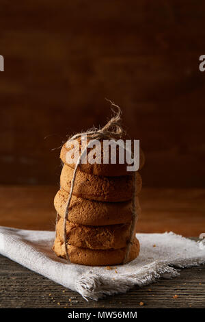 Biscotti fatti in casa tighted con un pezzo di corda sul tovagliolo homespun su un tavolo di legno, close-up, il fuoco selettivo. Pila di deliziosi biscotti. Natale Foto Stock