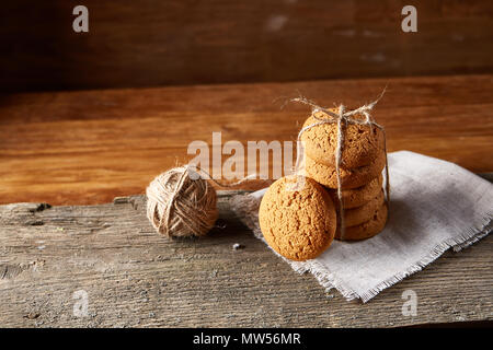 Biscotti fatti in casa tighted con un pezzo di corda sul tovagliolo homespun su un tavolo di legno, close-up, il fuoco selettivo. Pila di deliziosi biscotti. Natale Foto Stock