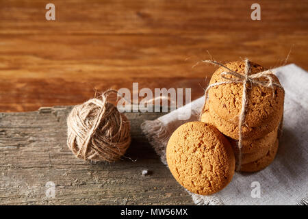 Biscotti fatti in casa tighted con un pezzo di corda sul tovagliolo homespun su un tavolo di legno, close-up, il fuoco selettivo. Pila di deliziosi biscotti. Natale Foto Stock