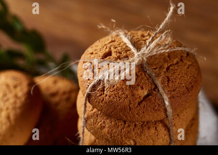 Composizione di natale con la pila di biscotti rimasto incastrato con nastro, bastoncini di cannella e asciugato le arance in luce sullo sfondo di legno, close-up. Festive concep Foto Stock