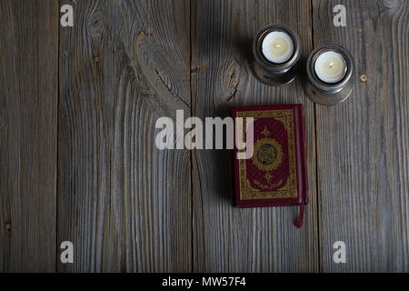 Corano e candele su una superficie di legno. Traduzione in inglese - il libro contiene versetti del Corano Foto Stock