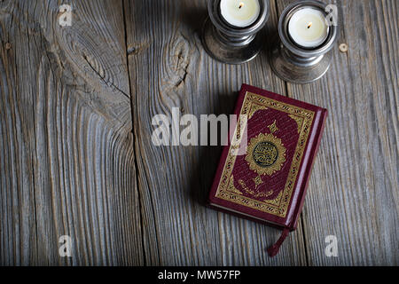 Corano e candele su una superficie di legno. Traduzione in inglese - il libro contiene versetti del Corano Foto Stock