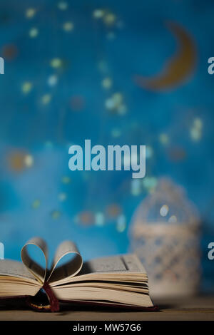 Il libro sacro del Corano su una superficie di legno. Notte Blu cielo con luna crescente e porta candele in background Foto Stock