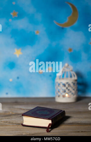 Il libro sacro del Corano su una superficie di legno. Notte Blu cielo con luna crescente e porta candele in background Foto Stock