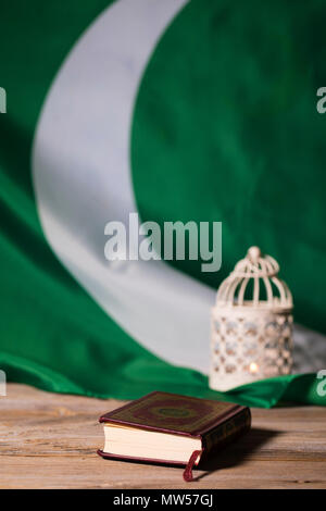Il libro sacro del Corano su una superficie di legno. Bandiera del Pakistan e porta candele in background. Traduzione - libro contiene versetti del Corano Foto Stock