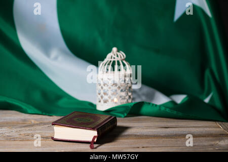 Il libro sacro del Corano su una superficie di legno. Bandiera del Pakistan e porta candele in background. Traduzione - libro contiene versetti del Corano Foto Stock