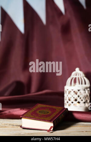 Il libro sacro del Corano su una superficie di legno. Bandiera del Qatar e porta candele in background Foto Stock