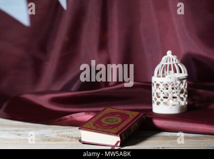 Il libro sacro del Corano su una superficie di legno. Bandiera del Qatar e porta candele in background. Tanslation- il libro contiene versetti del Corano. Foto Stock