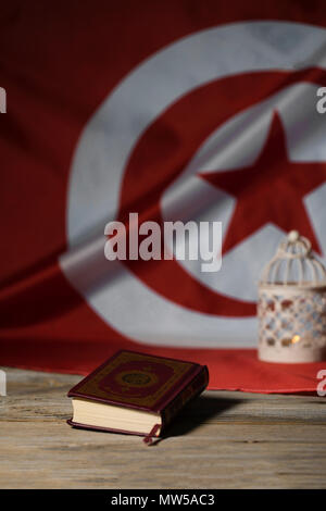 Il libro sacro del Corano su una superficie di legno. Bandiera tunisina e porta candele in background Foto Stock