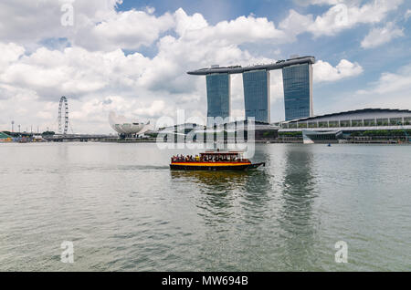 Una barca di crociera noto come twakows ride passa la famosa Marina Bay Sands Hotel. La barca sono stati utilizzati per scopi di trasporto lungo il Fiume Singapore. Foto Stock