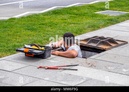 Lavorando in pozzetto, lavoratore di effettuare riparazioni su approvvigionamento di acqua in corrispondenza di una strada di città. Foto Stock