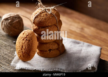 Biscotti fatti in casa tighted con un pezzo di corda sul tovagliolo homespun su un tavolo di legno, close-up, il fuoco selettivo. Pila di deliziosi biscotti. Natale Foto Stock