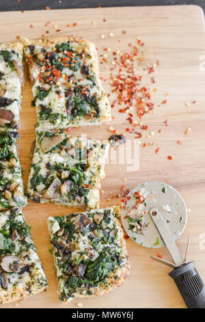 La cottura a vapore caldo stile di Detroit pizza con formaggio e spinaci topping di funghi, condite con peperoncino rosso e tagliare in quadrati. Foto Stock