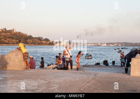 Le persone si radunano presso il porto di Havana, Cuba, Marzo 29, 2018 come il sole tramonta sull'Oceano Atlantico. La statua del Cristo in Casa Blanca è al top Foto Stock