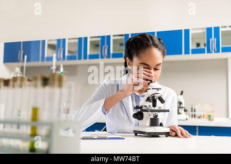 Giovane tecnico di laboratorio in camice bianco analisi di campioni mediante microscopio in laboratorio Foto Stock