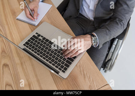 Vista aerea del businessman disabili lavorando su laptop e la scrittura nel notebook in ufficio Foto Stock