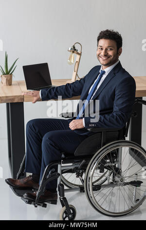 Disabilitato African American businessman guardando la fotocamera mentre è seduto al posto di lavoro con il computer portatile in ufficio Foto Stock