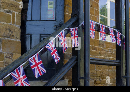Una fila di piccoli Union Jack infilate le bandiere lungo un corrimano in legno al di fuori di un village pub; grande Brington, Northamptonshire, Regno Unito Foto Stock