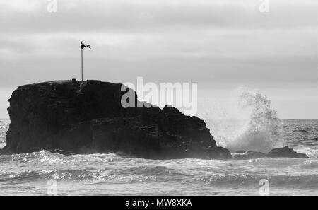 Perranporth Cappella, rock Cornish bandiera di St Pirran, volare sulla roccia, con un'onda di schiantarsi contro la roccia creando una curva di acqua bianca Foto Stock
