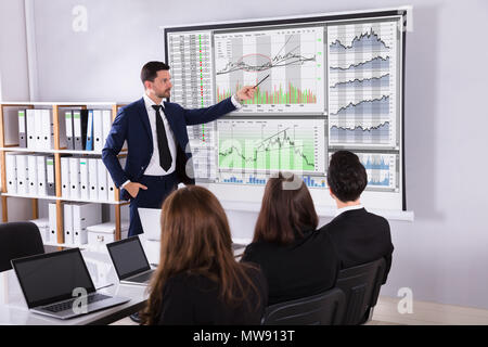 Giovane Maschio stock broker di mercato dando la presentazione al suo partner su un proiettore Foto Stock