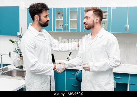 Professional giovani farmacisti in camici stringono le mani nel laboratorio scientifico Foto Stock